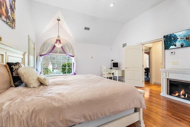 bedroom featuring a fireplace, wood finished floors, visible vents, and high vaulted ceiling