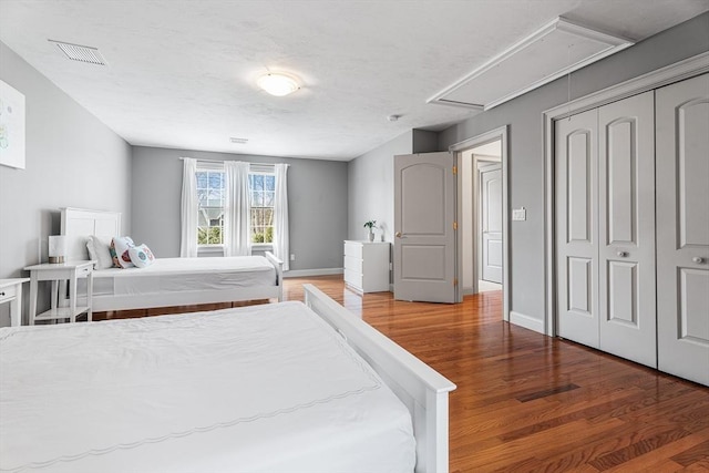 bedroom with visible vents, baseboards, a closet, attic access, and wood finished floors