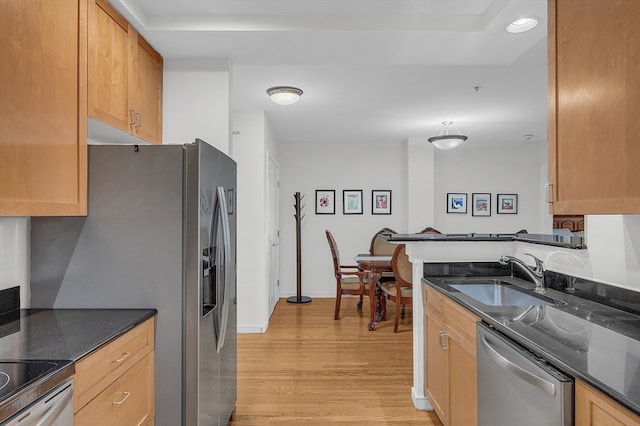 kitchen with kitchen peninsula, appliances with stainless steel finishes, sink, light hardwood / wood-style flooring, and dark stone countertops