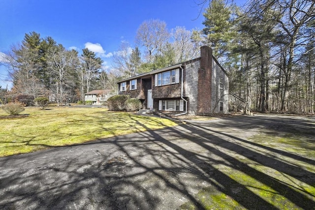 view of front facade with driveway, a chimney, and a front lawn