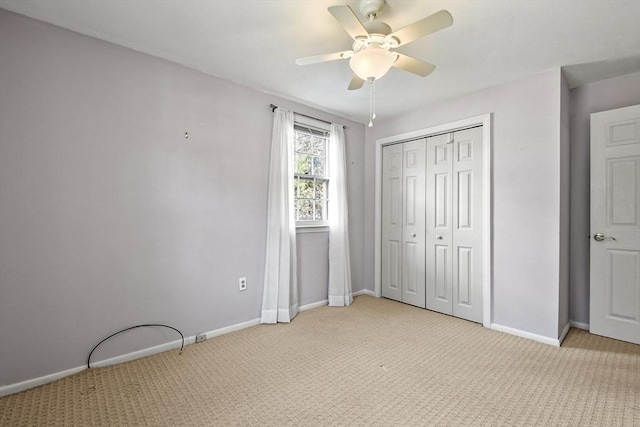 unfurnished bedroom featuring a ceiling fan, a closet, light carpet, and baseboards