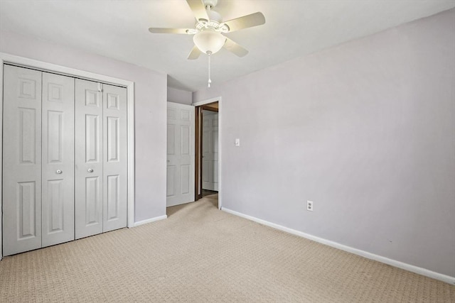 unfurnished bedroom with ceiling fan, a closet, light colored carpet, and baseboards