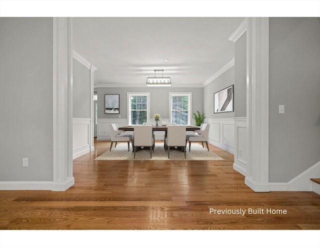dining area with crown molding, wainscoting, a decorative wall, and light wood finished floors
