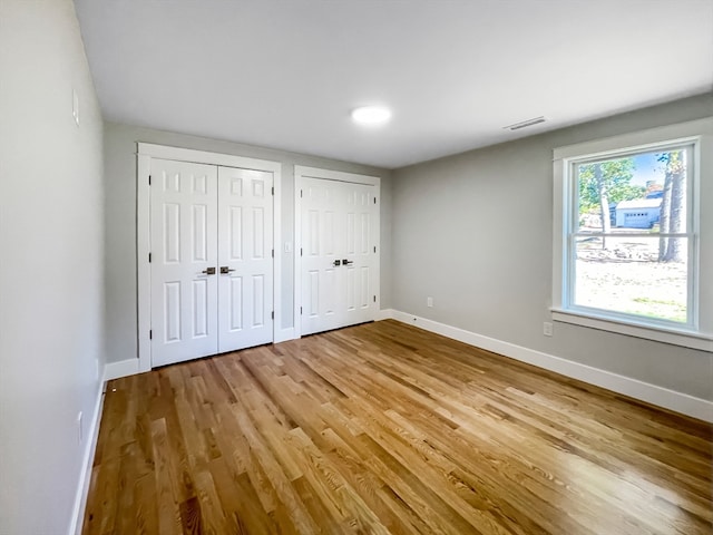 unfurnished bedroom with light wood-type flooring and two closets