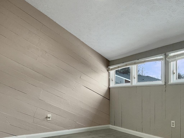 unfurnished room featuring a textured ceiling, baseboards, and wood finished floors