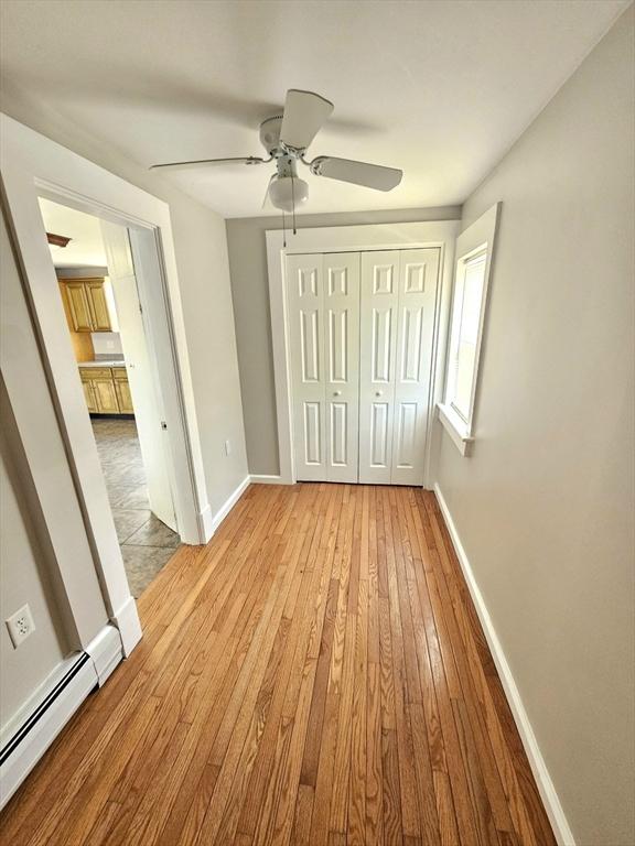 unfurnished bedroom with a closet, baseboard heating, light wood-type flooring, and baseboards