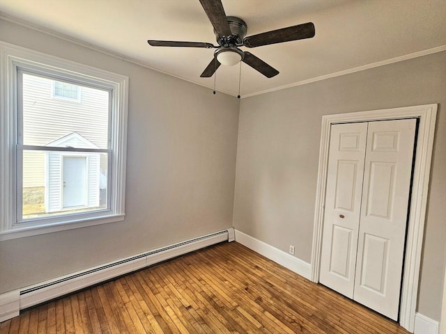 unfurnished bedroom featuring hardwood / wood-style floors, crown molding, baseboards, and a baseboard radiator