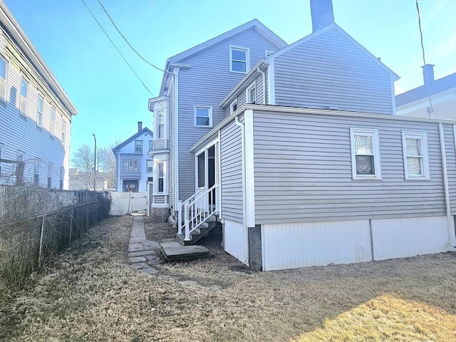 rear view of property with entry steps, a yard, and fence