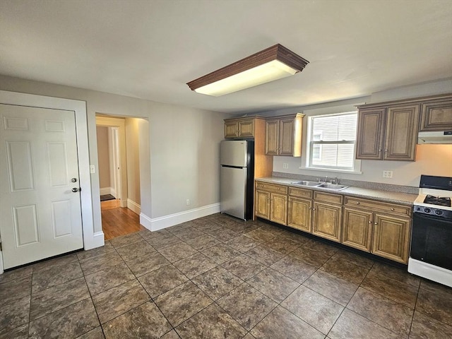 kitchen with range with gas stovetop, freestanding refrigerator, a sink, light countertops, and under cabinet range hood