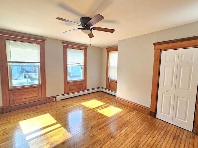 spare room featuring a ceiling fan, baseboards, light wood-type flooring, and a baseboard heating unit