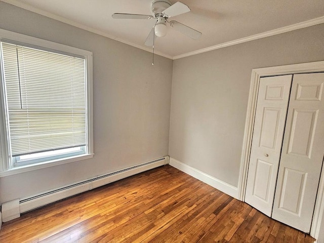 unfurnished bedroom with a closet, baseboard heating, ornamental molding, and hardwood / wood-style flooring