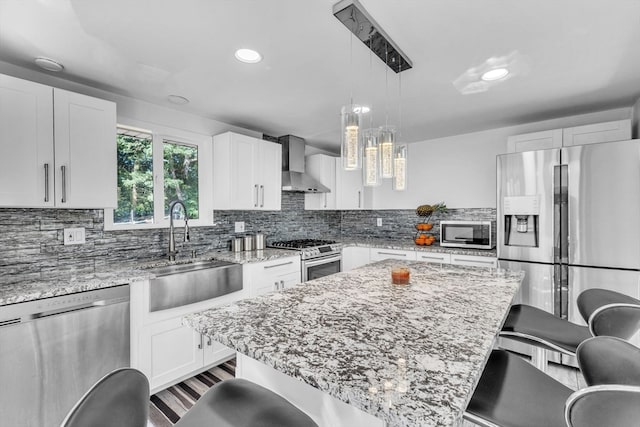 kitchen with sink, white cabinets, a kitchen bar, wall chimney exhaust hood, and appliances with stainless steel finishes