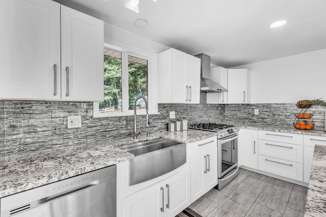 kitchen with sink, white cabinetry, wall chimney exhaust hood, stainless steel appliances, and light stone countertops