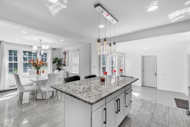 kitchen with a kitchen island, light stone countertops, pendant lighting, and white cabinets