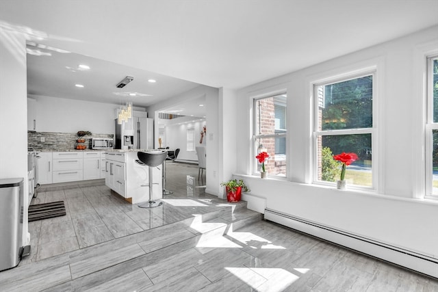 kitchen featuring white cabinets, a kitchen island, a baseboard heating unit, stainless steel appliances, and a breakfast bar