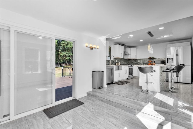 kitchen with hanging light fixtures, wall chimney range hood, white cabinetry, appliances with stainless steel finishes, and a breakfast bar