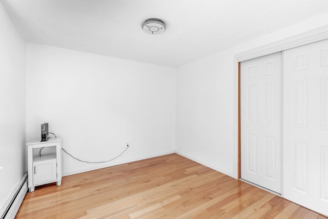 unfurnished bedroom with a baseboard radiator, light wood-type flooring, and a closet