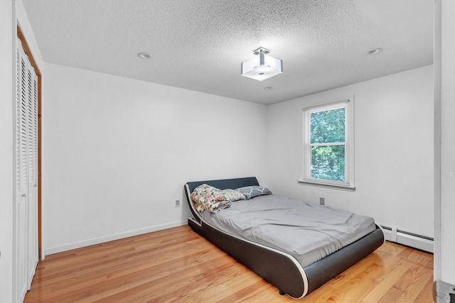 bedroom with a baseboard radiator, a closet, a textured ceiling, and hardwood / wood-style flooring