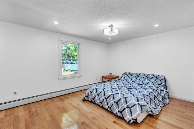 bedroom featuring a baseboard radiator, light hardwood / wood-style floors, and a textured ceiling