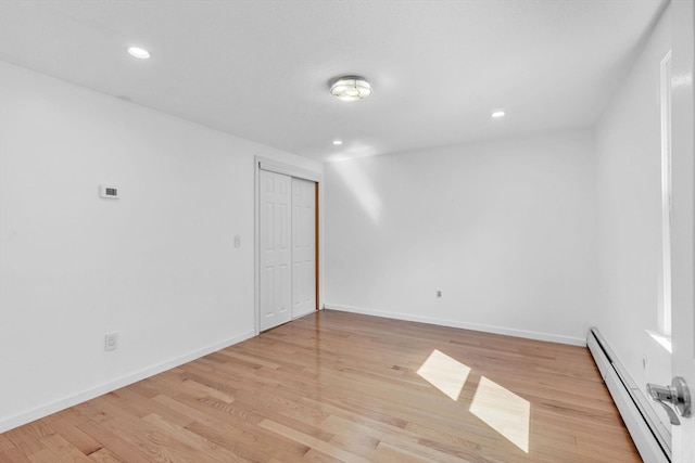 unfurnished room featuring a baseboard heating unit and light hardwood / wood-style flooring