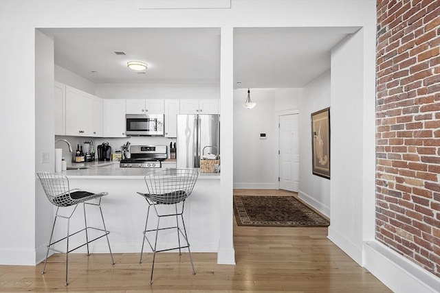 kitchen with white cabinetry, sink, kitchen peninsula, light hardwood / wood-style floors, and appliances with stainless steel finishes