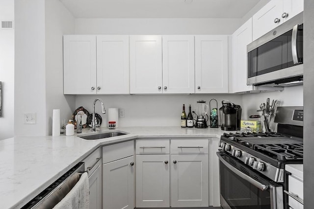 kitchen with appliances with stainless steel finishes, light stone counters, white cabinetry, and sink