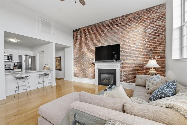 living room with ceiling fan, brick wall, and light hardwood / wood-style flooring