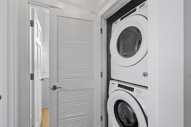 clothes washing area featuring stacked washing maching and dryer and crown molding