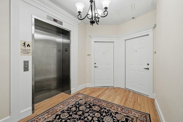 entryway with elevator, a chandelier, and light wood-type flooring