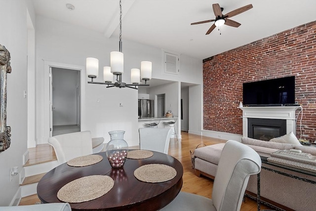 dining area featuring ceiling fan with notable chandelier, beam ceiling, light wood-type flooring, and brick wall