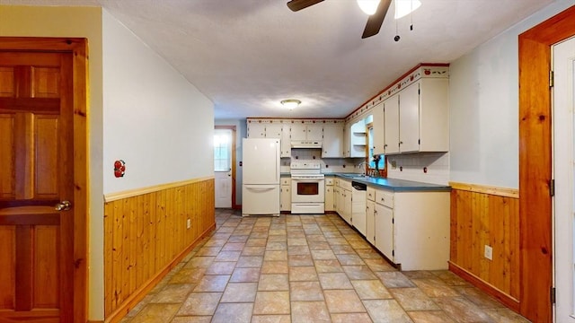 kitchen featuring white appliances, wooden walls, wainscoting, under cabinet range hood, and a sink