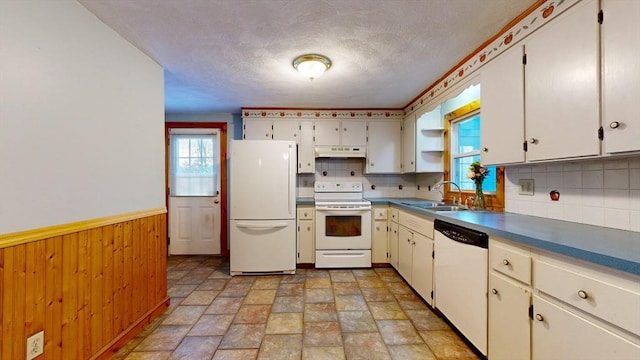 kitchen featuring white appliances, wainscoting, wood walls, under cabinet range hood, and a sink