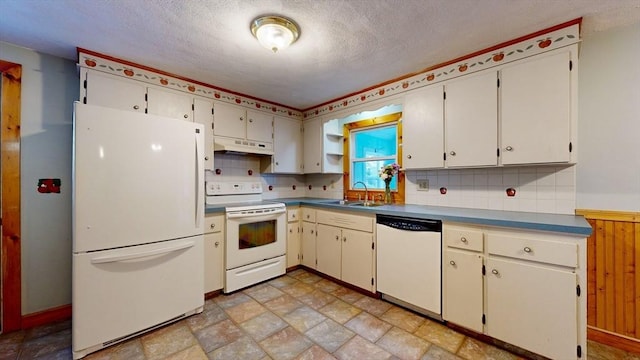 kitchen with white appliances, a sink, stone finish flooring, under cabinet range hood, and backsplash