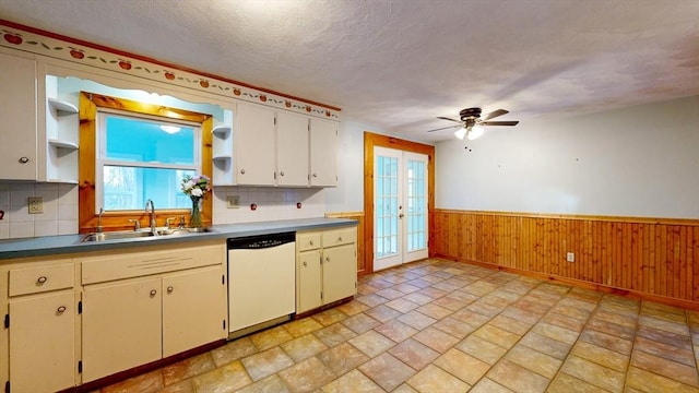 kitchen featuring open shelves, wainscoting, white dishwasher, a textured ceiling, and a sink