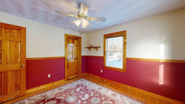 empty room featuring wainscoting, ceiling fan, baseboards, and wood finished floors