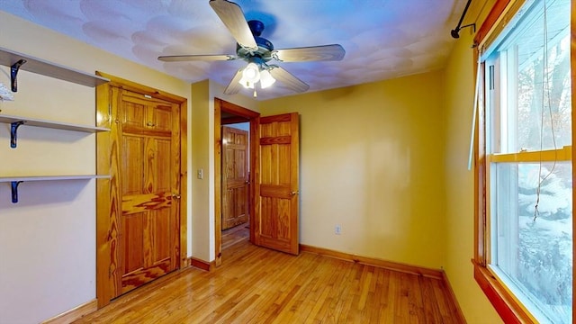 unfurnished bedroom featuring ceiling fan, multiple windows, light wood-style flooring, and baseboards