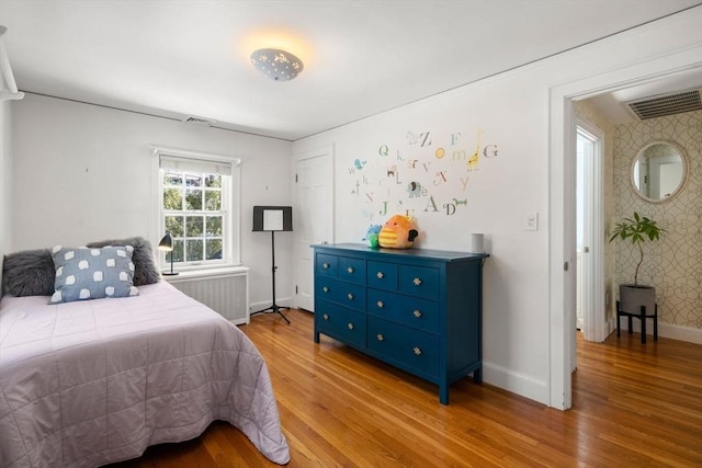 bedroom featuring visible vents, baseboards, light wood-style floors, radiator heating unit, and wallpapered walls