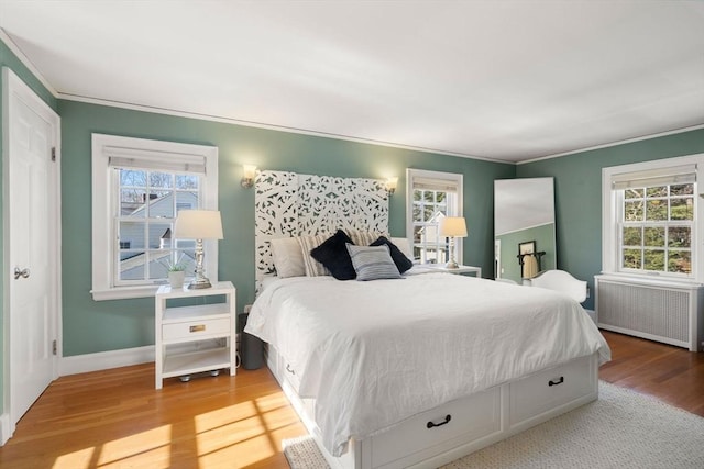 bedroom featuring ornamental molding, light wood finished floors, multiple windows, and radiator