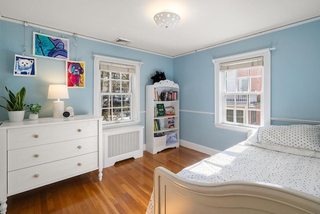 bedroom with baseboards, radiator heating unit, visible vents, and wood finished floors