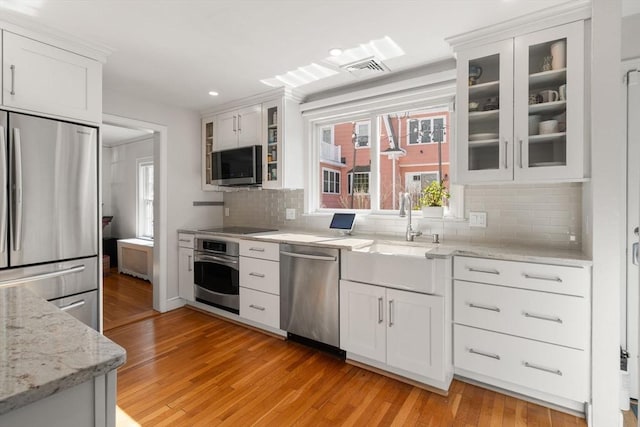 kitchen featuring light wood-style flooring, a sink, white cabinets, appliances with stainless steel finishes, and decorative backsplash