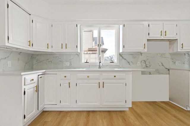 kitchen with light countertops, white cabinets, a sink, and light wood finished floors