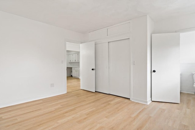 unfurnished bedroom featuring light wood-style flooring, baseboards, and a closet