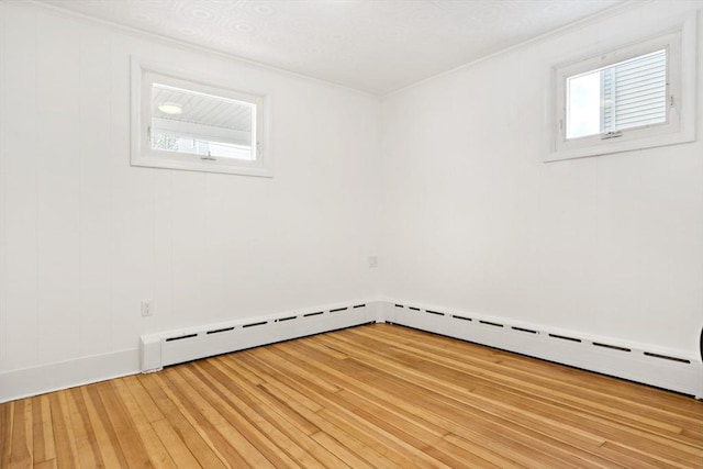 spare room featuring ornamental molding, baseboard heating, and light wood-type flooring