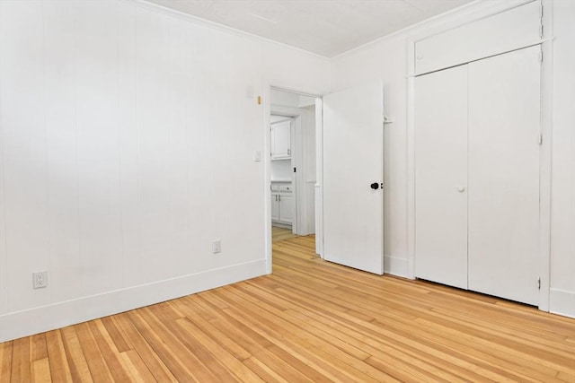 unfurnished bedroom with light wood-style flooring, ornamental molding, and a closet