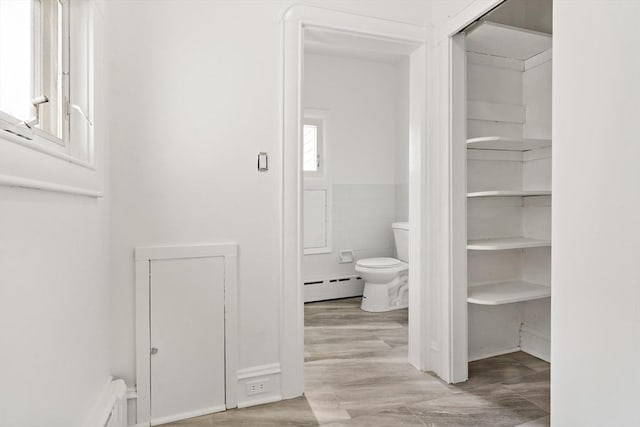 bathroom with toilet, a baseboard radiator, tile walls, and wood finished floors