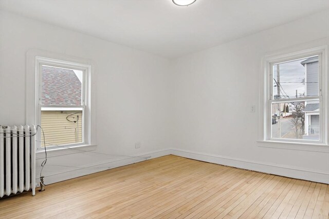 spare room featuring radiator, a healthy amount of sunlight, and hardwood / wood-style flooring