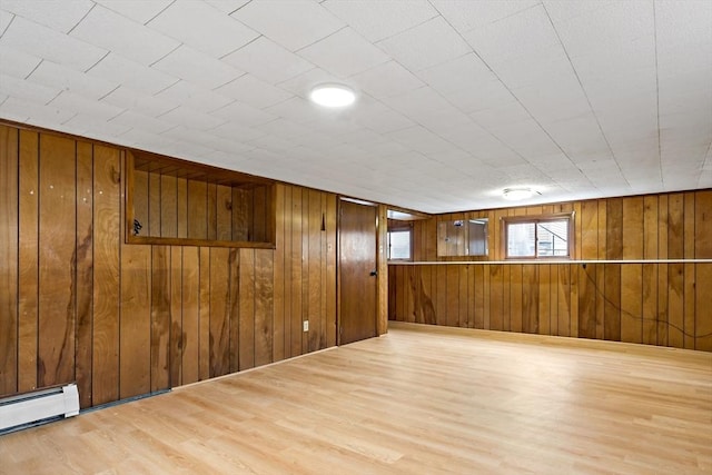 empty room with wood walls, a baseboard radiator, and wood finished floors