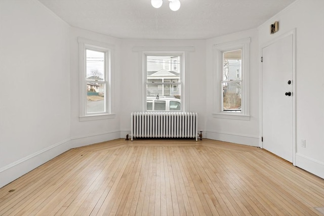 empty room with baseboards, radiator heating unit, and light wood-style floors