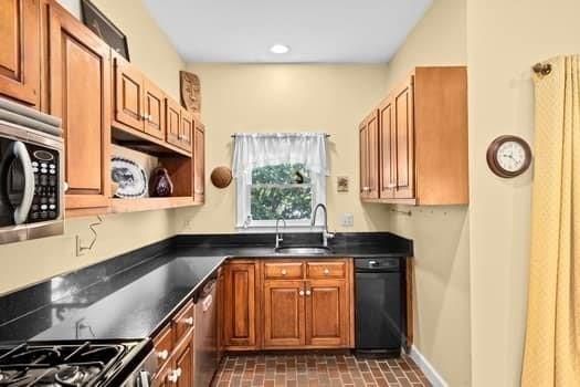 kitchen with a sink, appliances with stainless steel finishes, brown cabinets, and dark countertops