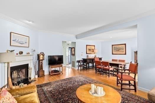living room featuring baseboards, a fireplace with flush hearth, ornamental molding, and wood finished floors